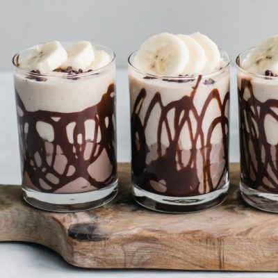 Peanut Butter, Chocolate & Banana Smoothie Shooters in Three Glasses on a Wooden Cutting Board