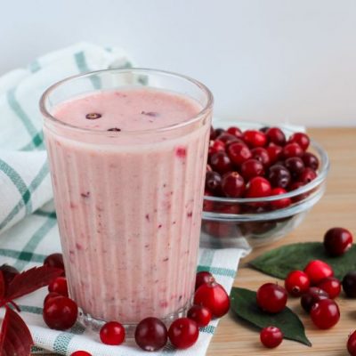 Cranberry smoothie in tall glass surrounded by fresh cranberries