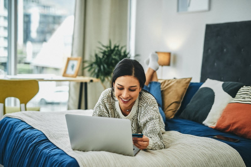 Smiling Woman Lying on Bed with Laptop Shopping Vitacost Black Friday Sale