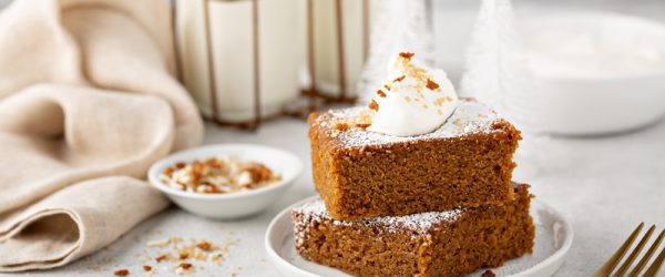 Two Slices of Gingerbread Cake Rest On a Small Plate Topped With Powdered Sugar and a Dollop of Whipped Cream.