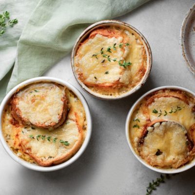 Top Shot of Gratineed Cheese and Toast on Top of Homemade French Onion Soup in Ramekins on Linen Table Cloth
