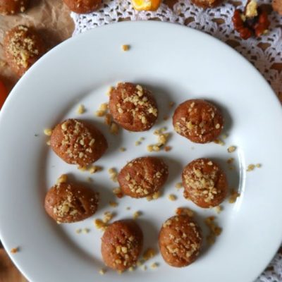 Melomakarona (Greek Christmas Honey Cookies) on a round serving plate surrounded by walnuts and orange slices
