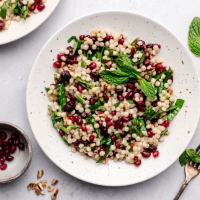 Festive Pomegranate Couscous Salad with Mint, Spinach and Cranberries on Stoneware Plate