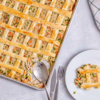 Overhead Shot of Sheet Pan Chicken Pot Pie with a Golden-Brown Lattice Pastry Crust Criss-Crossing the Top. One Slice is Cut Out and Presented on a Round White Plate