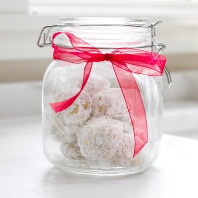 A Glass Jar With Rubber Seal and Red Bow is Filled With Einkorn Snowball Cookies With Walnuts.