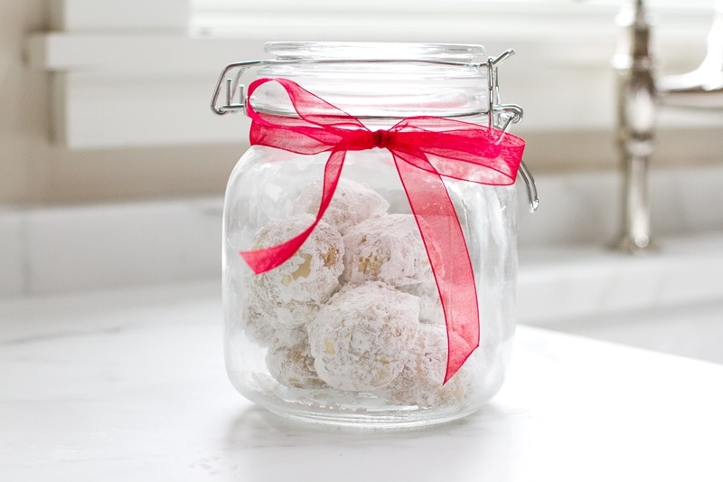 A Glass Jar With Rubber Seal and Red Bow is Filled With Einkorn Snowball Cookies With Walnuts.