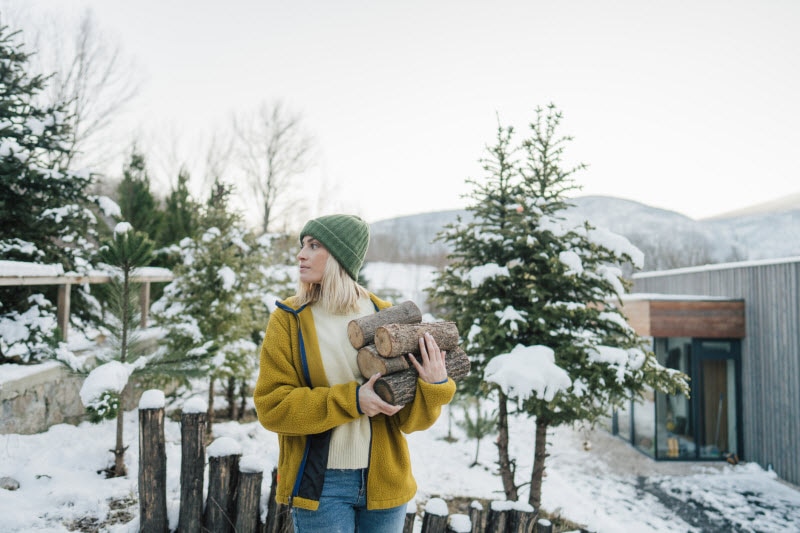 Woman Gathering Firewood Outside Her Home Practicing Winter Sustainability Tips