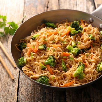 Asian Shiritaki Noodles & Veggies in Skillet on Wooden Table Top with Chopsticks Nearby