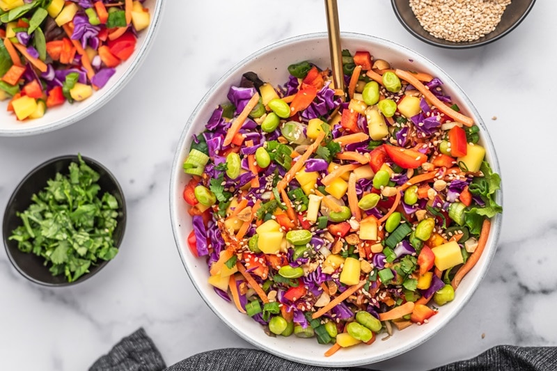 A Colorful Chopped Thai Salad Fills a White Bowl With Small Bowls of Cilantro and Sesame Seeds on the Side.