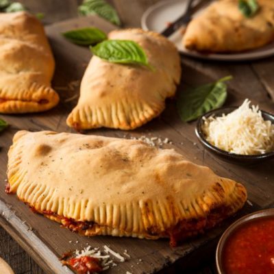 Gluten-Free Mini Calzones Bursting at the Seams with Pizza Sauce on a Wooden Cutting Board