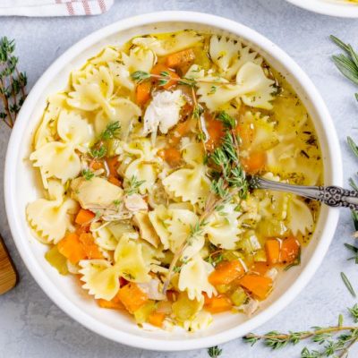 Comforting Homemade Chicken Noodle Soup in a Large Bowl With a Waiting Spoon, Sprigs of Rosemary & Thyme Surround it