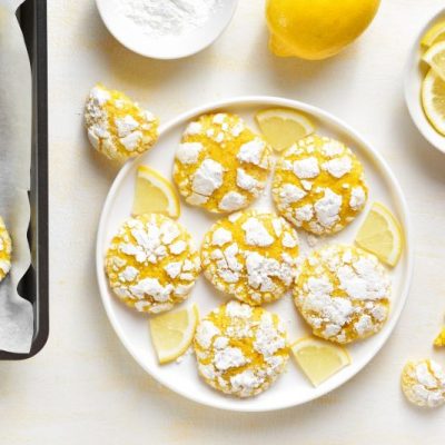 Lemon Crinkle Cookies Dusted in Powdered Sugar Set on Plate with Lemon Slices