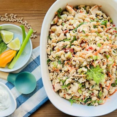 Veggie-Loaded Tuna Pasta Salad in Oval Serving Bowl Surrounded by Fresh Lime Slices, Dill, Scallions and a Bowl of Creamy Greek Yogurt