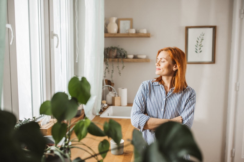 Woman With Her Eyes Closed at Kitchen Counter Thinking About Different Types of Rest to Restore Her Wellness