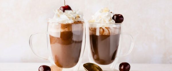 Cherry Almond Hot Chocolate_Resized Image_Loren Runion Two Tall Glass Mugs of Dairy-Free Cherry Almond Hot Chocolate with Whopped Cream and a Cherry on Top with two Gold Long-Handled Spoons Nearby