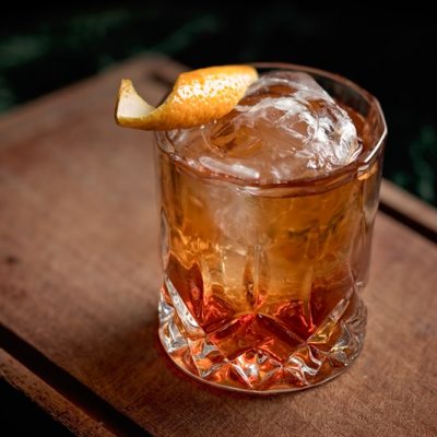 A Short Cocktail Glass is Filled With Brown Liquid and Garnished With a Twisted Orange Peel, Representing an Old Fashioned Mocktail Recipe.