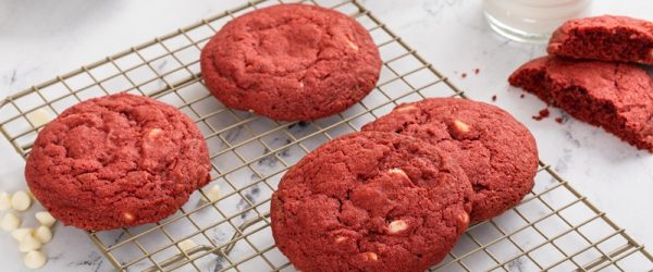 Red Velvet White Chocolate Chip Cookies Red Velvet White Chocolate Chip Cookies Sit on a Cooling Rack Next To White Chocolate Chips and a Glass of Milk.
