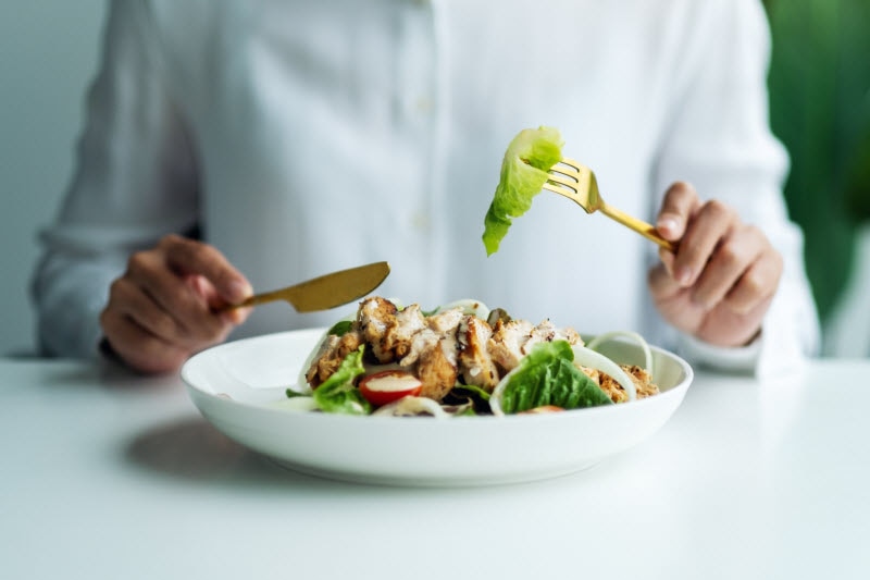 Torso View of Woman in White Blouse Eating Salad With Chicken to Represent Concept of Slow Digestion