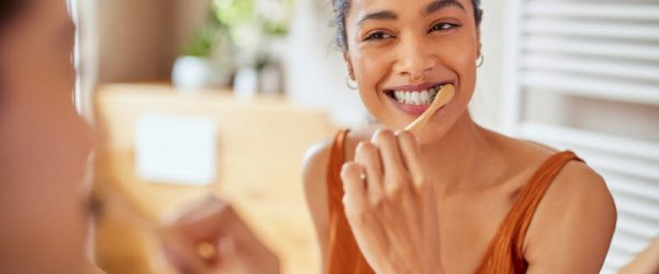 Woman Using Natural Teeth Whitening Toothpaste Smiling and Brushing Teeth While Looking in Mirror