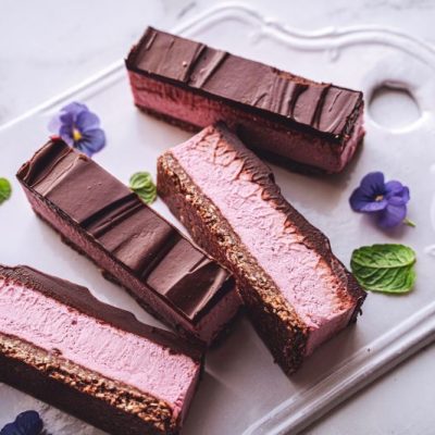 Strawberry Cheesecake Bars With Chocolate Ganache Set on a White Ceramic Serving Tile with Scattered Flowers