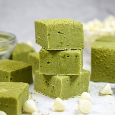 Close-up of White Chocolate Matcha Fudge Squares on Countertop Surrounded by White Chocolate Chips and a Glass Bowl of Matcha Powder