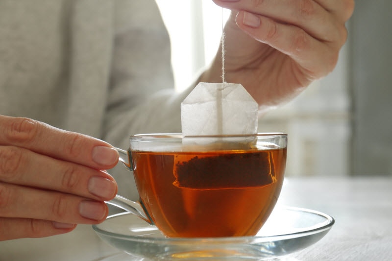 Concept of Microplastics Tea Bags Represented by Woman Dunking Tea Bag in Clear Mug