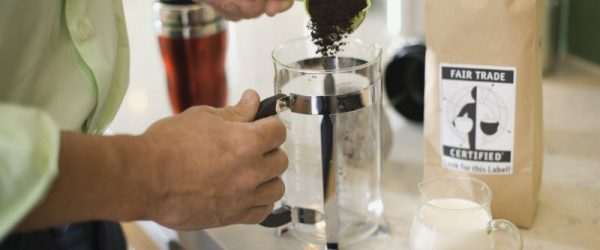 Person Scooping Grounds From Fair Trade Coffee Bag With Sustainability Certification on Label Into French Press