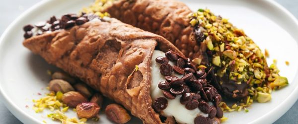 Two Gluten Free Cannolis Sit on a Plate, One Topped With Pistachios and the Other Topped With Mini Chocolate Chips.