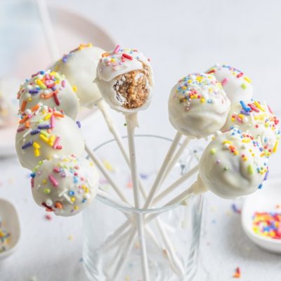 A Short Glass is Filled With Nine No Bake Cake Pops Covered in Rainbow Sprinkles.