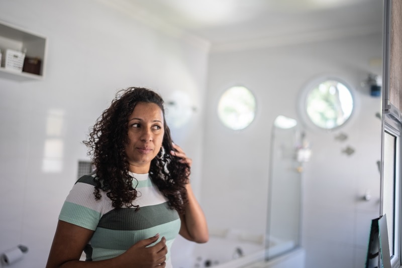 A Woman Examines Her Hair in the Mirror, Representing the Question, "Can Diabetes Cause Hair Loss?"