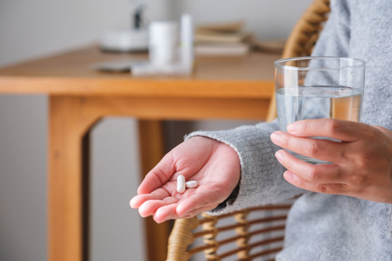 Torso View of Woman Holding Supplement Capsules in Hand With Glass of Water to Represent Concept Can Vitamins Make You Tired