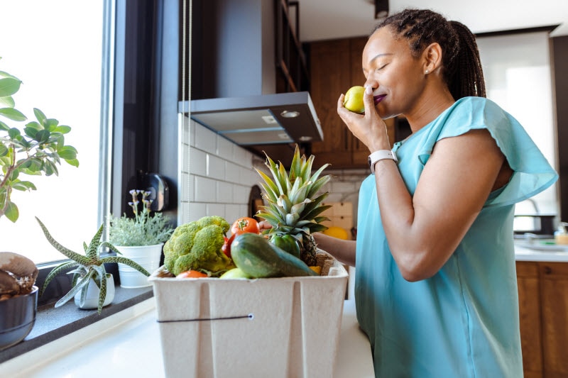 Woman Standing at Kitchen Counter Smelling Fresh Produce to Represent Concept of Best Vitamins for Menopause