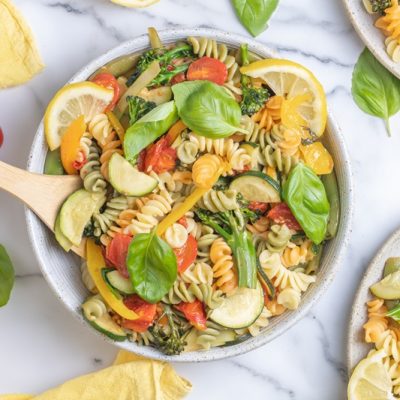 A Bowl is Filled With Pasta Primavera and Topped With Fresh Basil Leaves and Thin Lemon Slices.