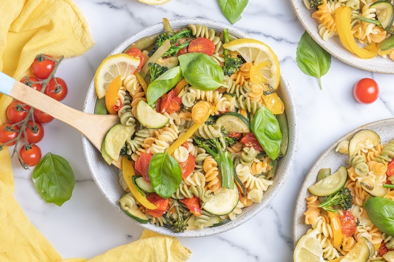 A Bowl is Filled With Pasta Primavera and Topped With Fresh Basil Leaves and Thin Lemon Slices.