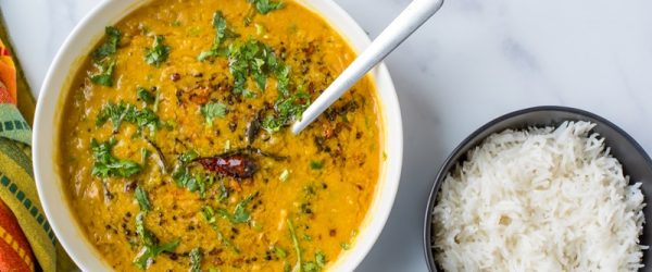 A Bowl of Red Lentil Dahl With Coconut Milk is Garnished With Cilantro, Pepper and Spices, Sits Beside a Bowl of White, Fluffy Basmati Rice.