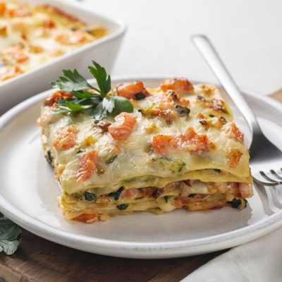 A Slice of Salmon Lasagna Sits on a Small, White Plate With a Sprig of Parsley.