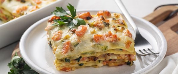 A Slice of Salmon Lasagna Sits on a Small, White Plate With a Sprig of Parsley.