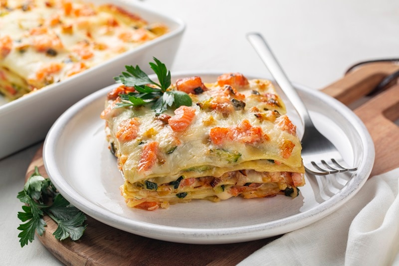 A Slice of Salmon Lasagna Sits on a Small, White Plate With a Sprig of Parsley.