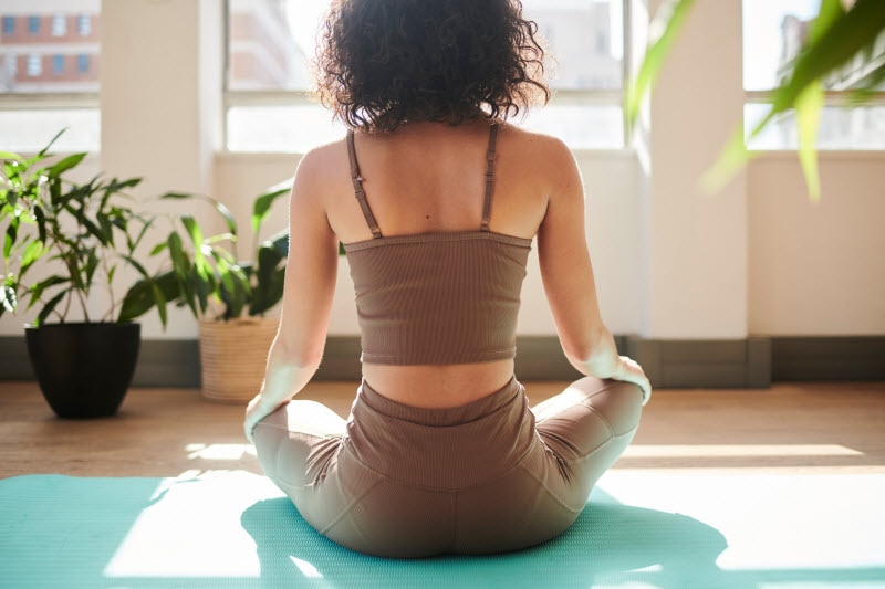 Back View of Woman on Mat in Living Room to Represent the Concept of Hidden Dangers of Yoga