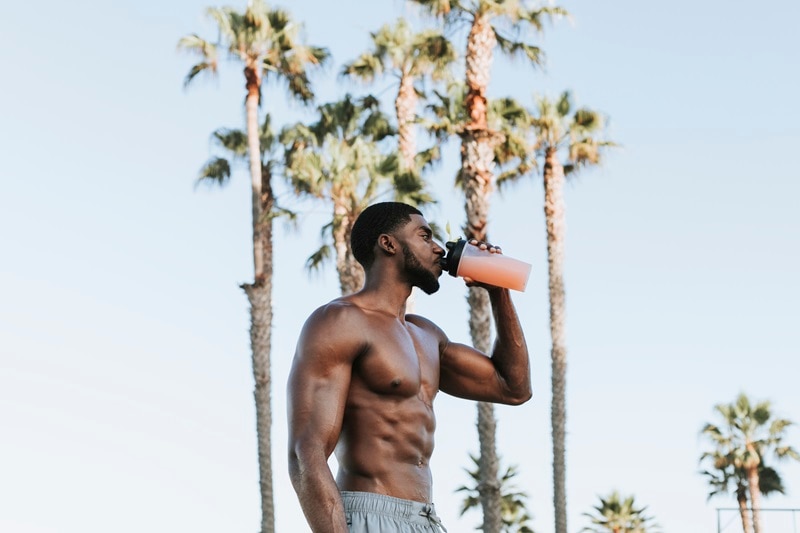 A Muscular Man Drinks a Beverage Outdoors, Representing the Question, "What Are Amino Acids?"