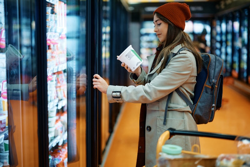 Woman Pleased With Idea of Food Dye Ban Standing In Front of Grocery Case Smiling While Reading a Product Label
