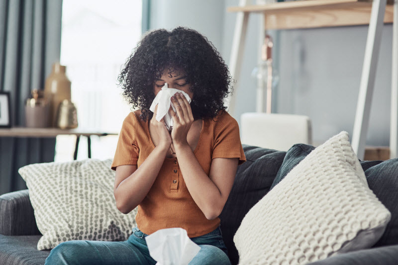 Concept of What is Hay Fever Represented by Woman Sitting on Living Room Couch Blowing Nose