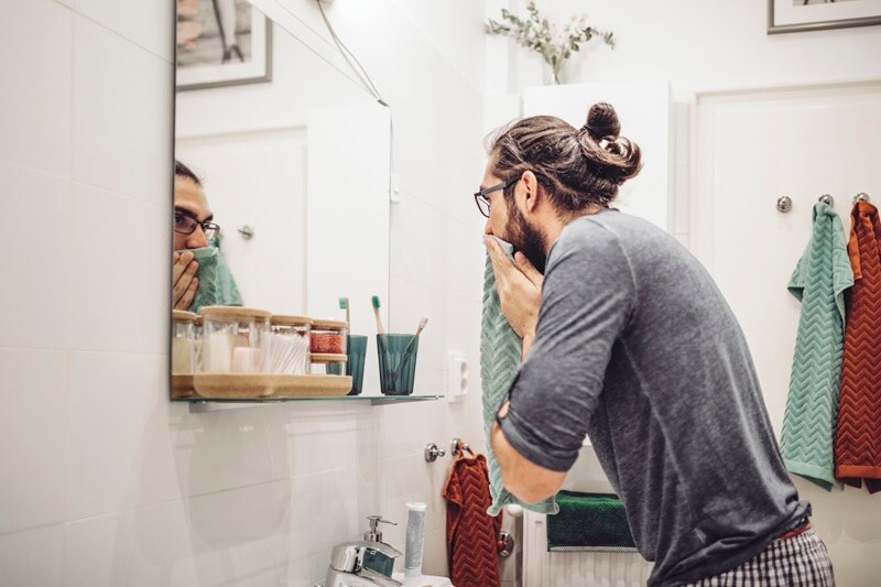 A Man Dries His Face at a Bathroom Mirror, Representing the Question, "What is a Facial Cleanser?"