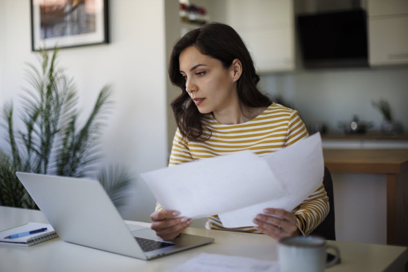 Woman Curious About What's a Lipid Panel Looking at Paperwork While Checking Information on Her Laptop