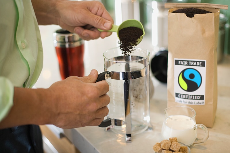World Fair Trade Day - Making a Difference, One Purchase at a Time Person Scooping Coffee Grounds into French Press to Represent World Fair Trade Importance