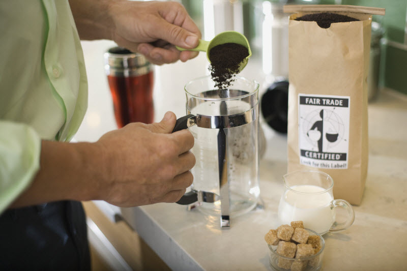 Person Scooping Coffee Grounds into French Press to Represent World Fair Trade Importance