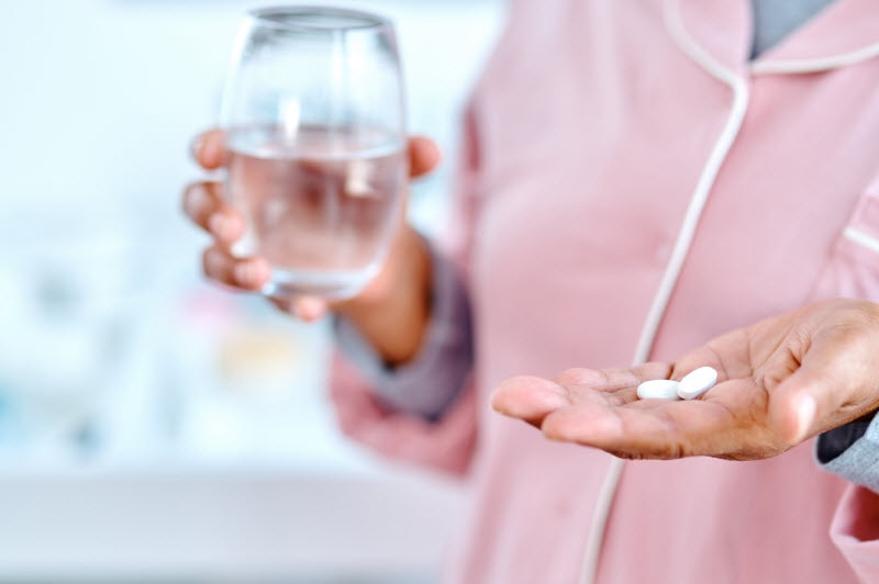 Torso View of Women in Pink Jacket Holding Glass of Water and Vitamins to Represent Concept of Best Supplements for Menopause