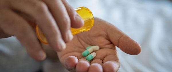 A Man Pours Antibiotic Capsules into His Hand, Representing the Relationship Between Antibiotics and Gut Health.