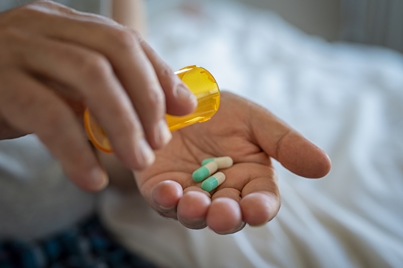 A Man Pours Antibiotic Capsules into His Hand, Representing the Relationship Between Antibiotics and Gut Health.