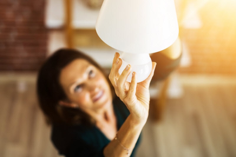 Overhead View of Woman Screwing in Lightbulb on Hanging Lamp to Represent Concept of Are LED Lights Bad for You